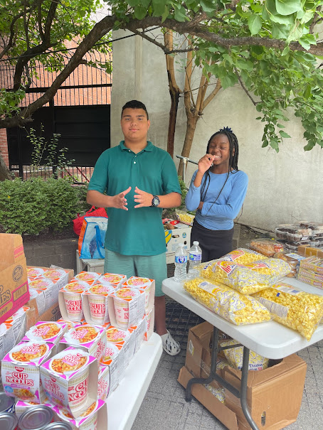 Young volunteers standing beside prepared noodles and snack supplies during outreach setup